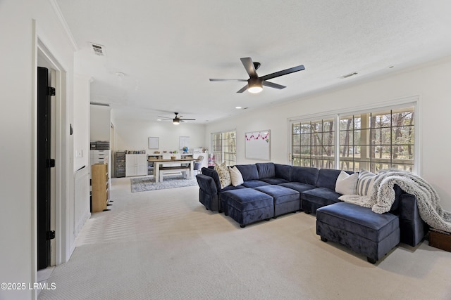 carpeted living area featuring visible vents, a ceiling fan, and ornamental molding