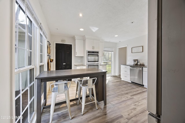 kitchen with light wood finished floors, tasteful backsplash, appliances with stainless steel finishes, white cabinetry, and recessed lighting