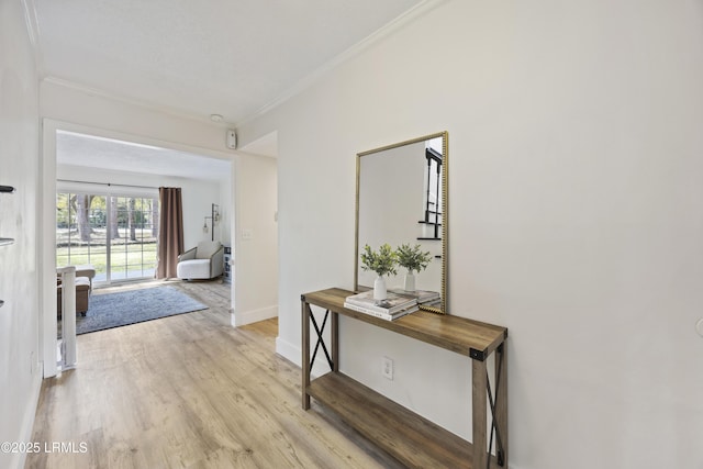 hall featuring light wood-type flooring, crown molding, and baseboards