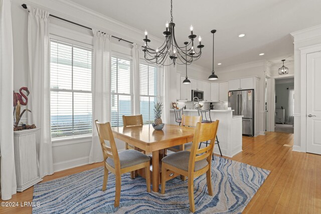 dining space with crown molding, an inviting chandelier, and light wood-type flooring