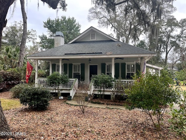 view of front facade featuring covered porch, ceiling fan, a chimney, and a shingled roof