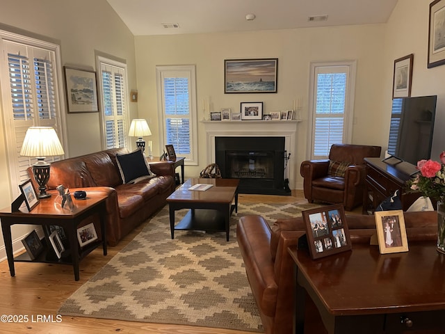 living area featuring lofted ceiling, visible vents, wood finished floors, and a glass covered fireplace