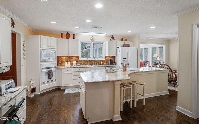 kitchen with white appliances, dark wood-type flooring, white cabinetry, light stone countertops, and a kitchen island