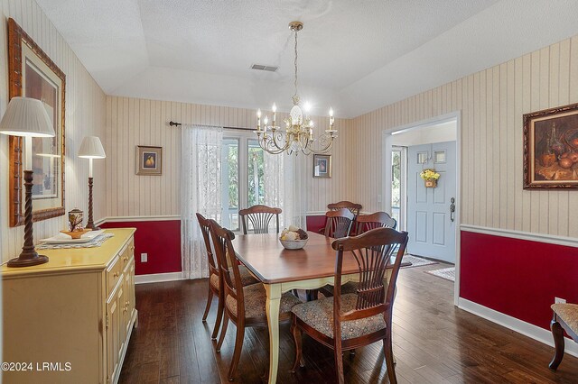 dining space featuring dark wood-type flooring, a tray ceiling, a chandelier, and a textured ceiling