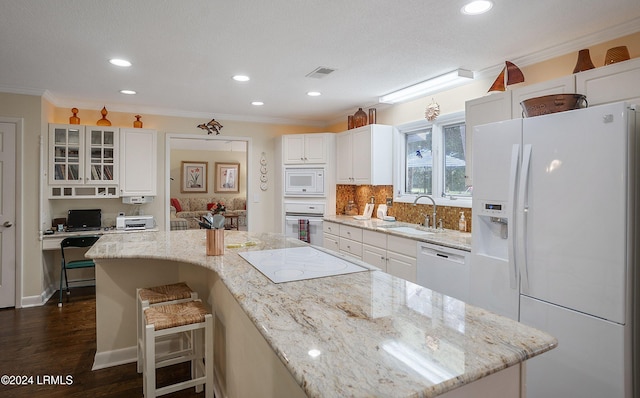 kitchen featuring sink, light stone counters, white cabinetry, a kitchen breakfast bar, and white appliances