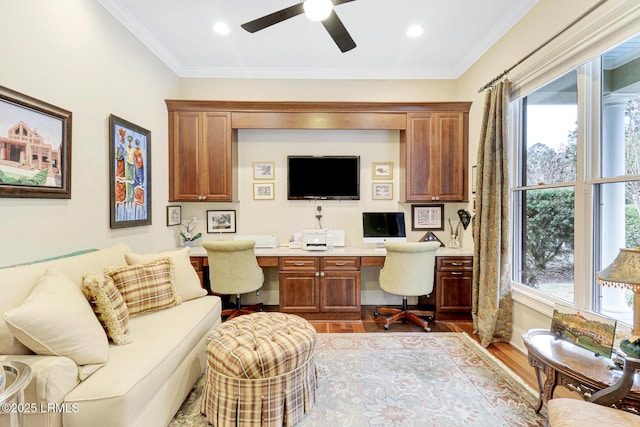 office space featuring ceiling fan, ornamental molding, built in desk, and light hardwood / wood-style floors