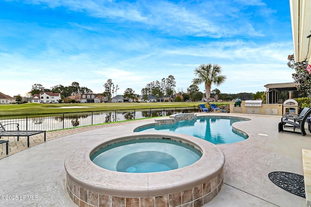 view of pool featuring a patio area, an outdoor kitchen, a water view, and an in ground hot tub