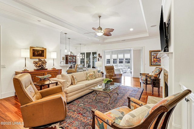 living room featuring ceiling fan, light hardwood / wood-style floors, and a tray ceiling