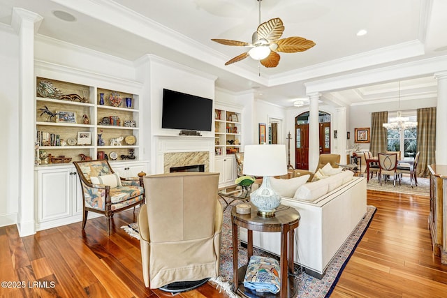 living room featuring crown molding, light hardwood / wood-style flooring, built in features, a high end fireplace, and decorative columns