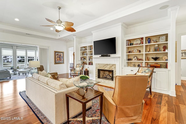 living room with built in shelves, a fireplace, ornamental molding, and hardwood / wood-style flooring