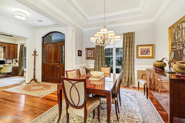 dining space featuring crown molding, decorative columns, a tray ceiling, wood-type flooring, and a chandelier