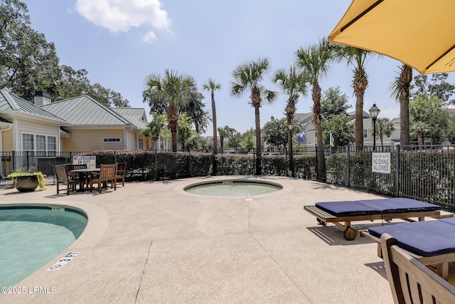 community pool with a patio area, fence, and a hot tub