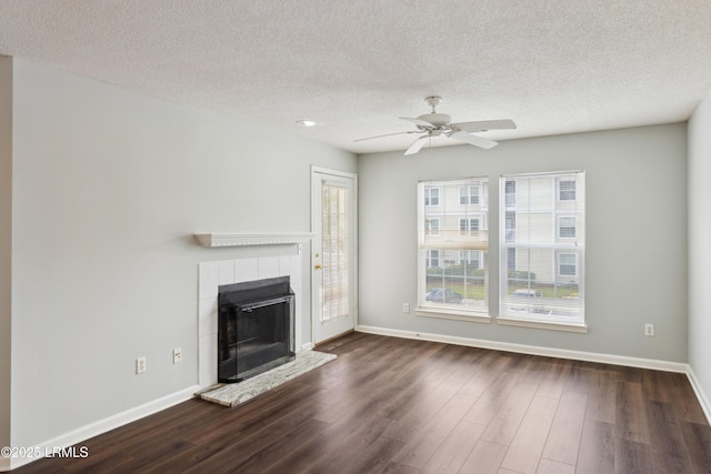 unfurnished living room with ceiling fan, baseboards, dark wood-style floors, and a tiled fireplace