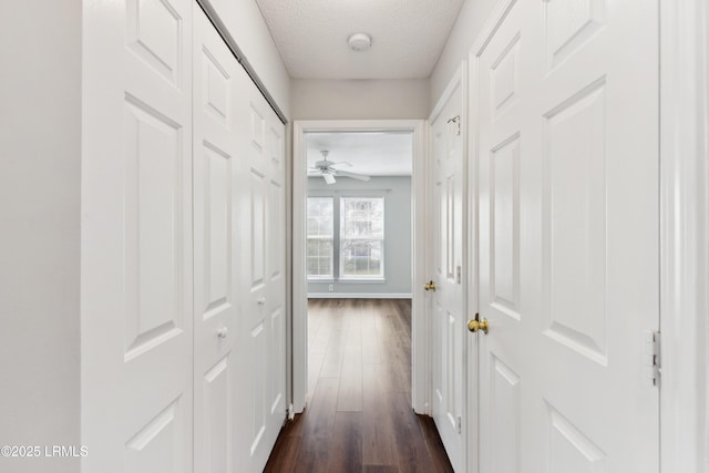 corridor with dark wood-type flooring, baseboards, and a textured ceiling