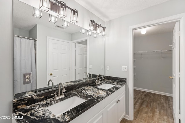 full bath with a textured ceiling, wood finished floors, a walk in closet, and a sink