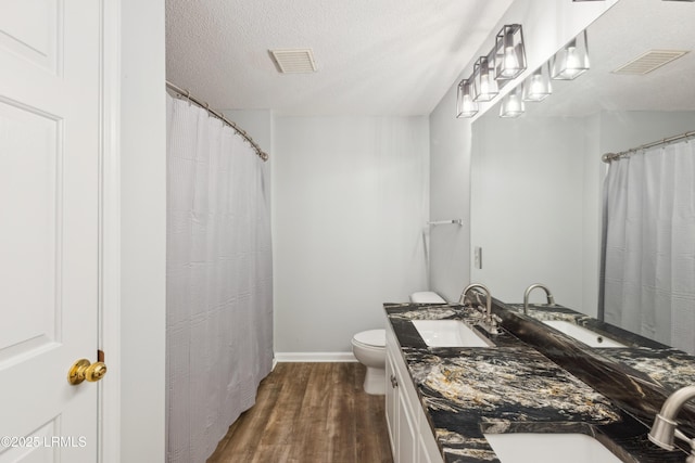 full bathroom featuring wood finished floors, visible vents, a sink, a textured ceiling, and toilet