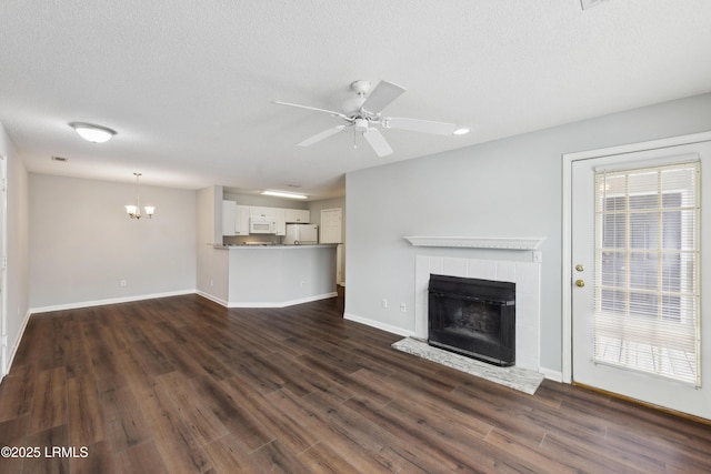 unfurnished living room featuring baseboards, a tiled fireplace, dark wood finished floors, ceiling fan with notable chandelier, and a textured ceiling