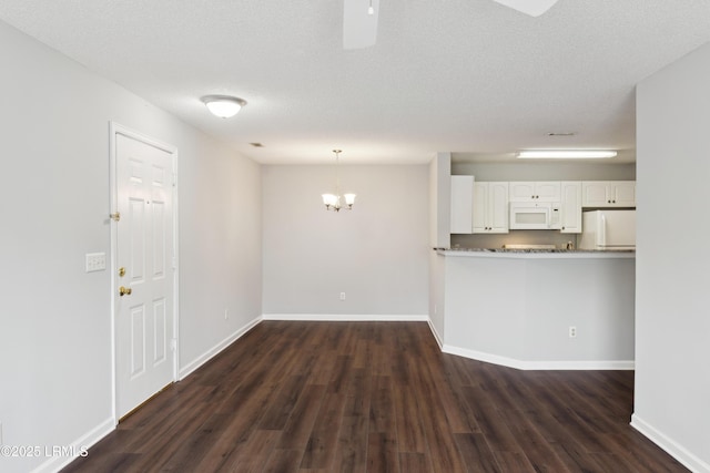 unfurnished living room with a chandelier, baseboards, a textured ceiling, and dark wood finished floors