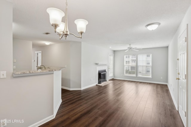 unfurnished living room with dark wood-style floors, a glass covered fireplace, ceiling fan with notable chandelier, and baseboards