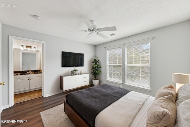 bedroom with visible vents, dark wood-type flooring, baseboards, ensuite bathroom, and a sink