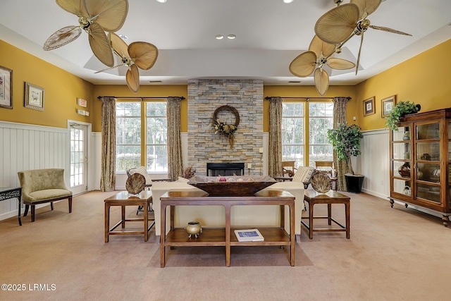 living room featuring light colored carpet, a fireplace, wainscoting, and a ceiling fan