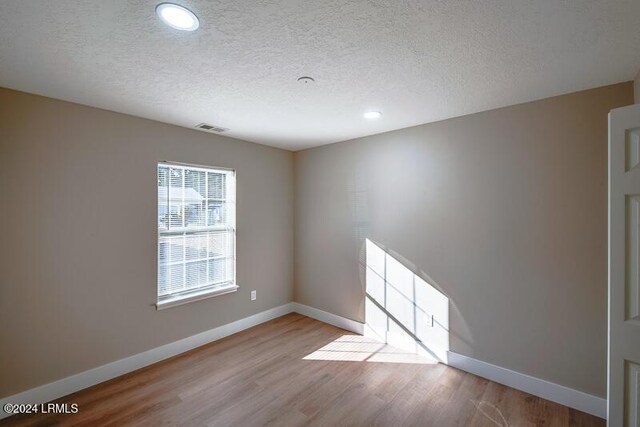 spare room featuring light hardwood / wood-style floors and a textured ceiling