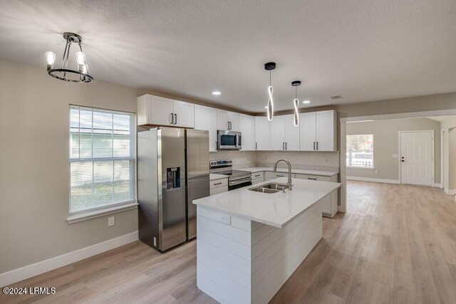 kitchen with sink, appliances with stainless steel finishes, hanging light fixtures, white cabinets, and a center island with sink