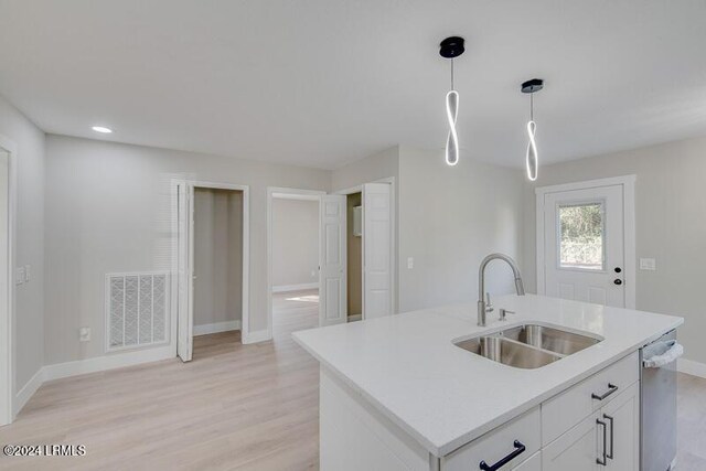 kitchen featuring sink, white cabinets, hanging light fixtures, stainless steel dishwasher, and a center island with sink