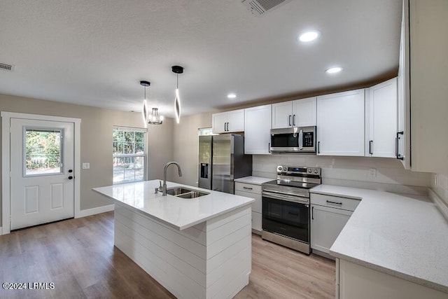 kitchen with sink, appliances with stainless steel finishes, an island with sink, white cabinets, and decorative light fixtures