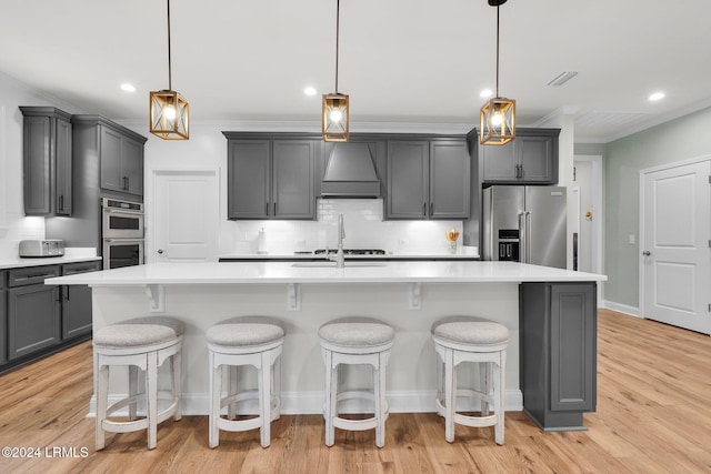 kitchen featuring premium range hood, decorative light fixtures, and a center island with sink