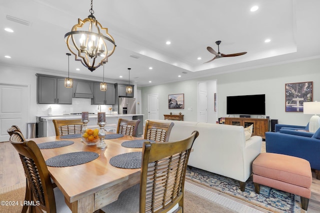 dining area featuring ornamental molding, light hardwood / wood-style flooring, ceiling fan with notable chandelier, and a tray ceiling