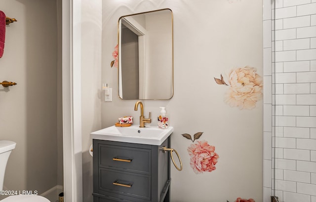 bathroom featuring vanity, a tile shower, and toilet