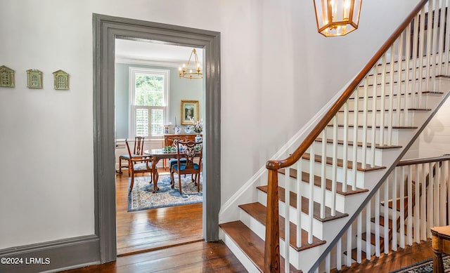 stairway with hardwood / wood-style flooring, ornamental molding, and a chandelier