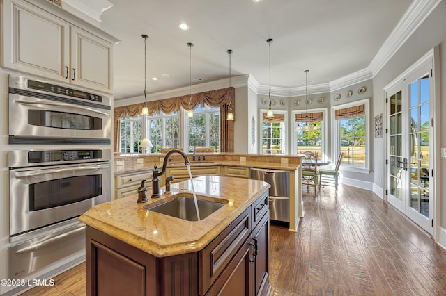 kitchen featuring hanging light fixtures, an island with sink, sink, and stainless steel double oven