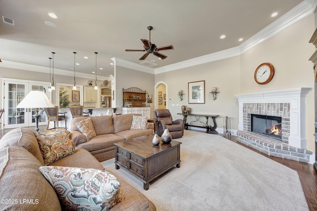 living room with hardwood / wood-style flooring, ceiling fan, ornamental molding, and a fireplace