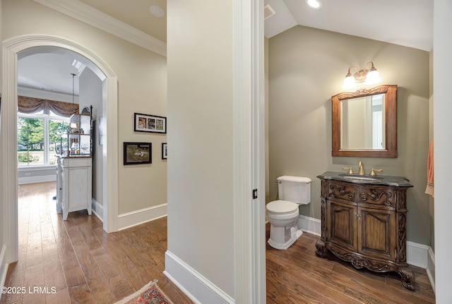 bathroom with vaulted ceiling, hardwood / wood-style flooring, vanity, ornamental molding, and toilet