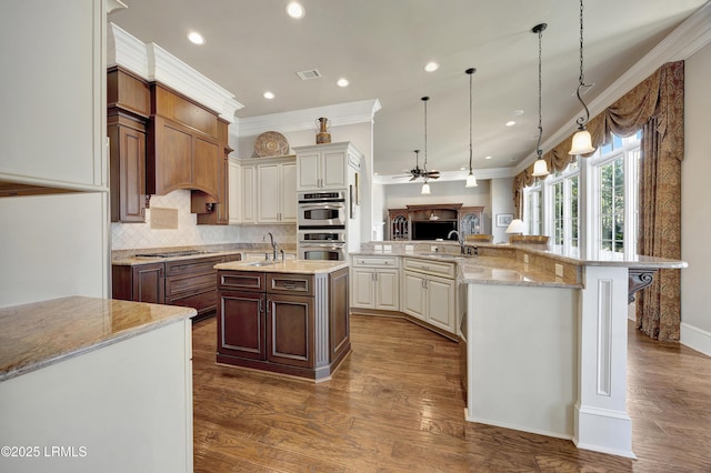 kitchen featuring a large island, hanging light fixtures, ornamental molding, light stone countertops, and a kitchen bar