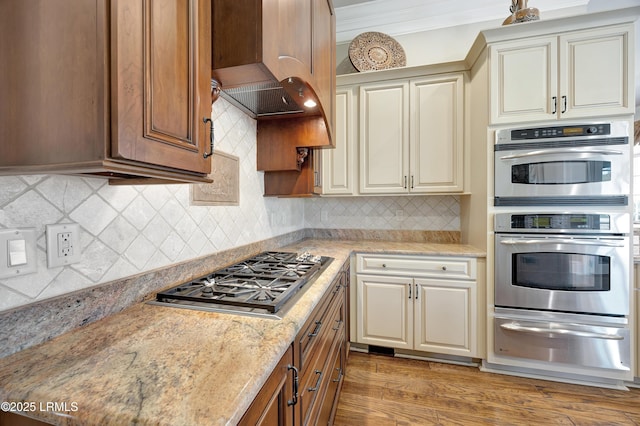 kitchen featuring crown molding, wood-type flooring, cream cabinetry, stainless steel appliances, and backsplash