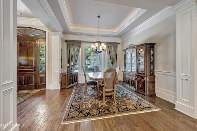 dining area featuring ornamental molding, dark hardwood / wood-style flooring, a raised ceiling, and a notable chandelier