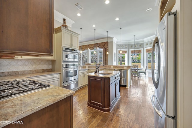 kitchen with sink, appliances with stainless steel finishes, a center island with sink, decorative light fixtures, and cream cabinetry