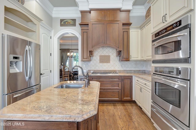 kitchen with sink, ornamental molding, stainless steel appliances, and a center island with sink