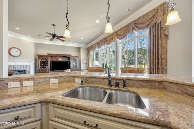 kitchen featuring pendant lighting, sink, light stone counters, ornamental molding, and cream cabinetry