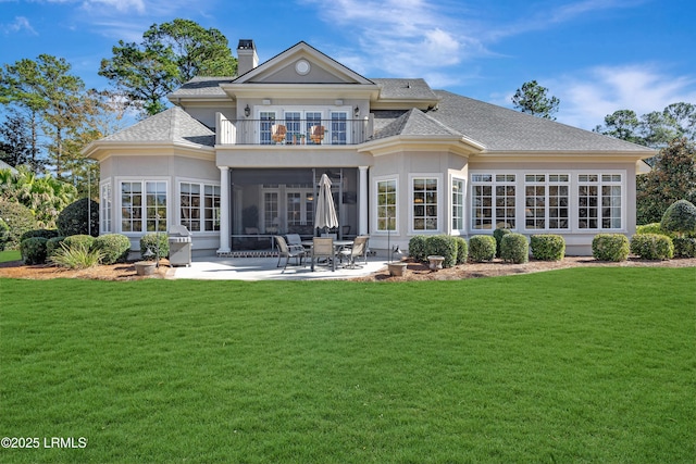 back of property with a balcony, a yard, a patio area, and a sunroom