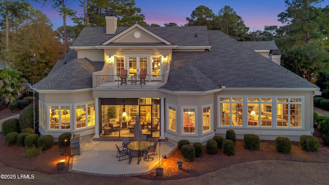 back house at dusk with a balcony and a patio area