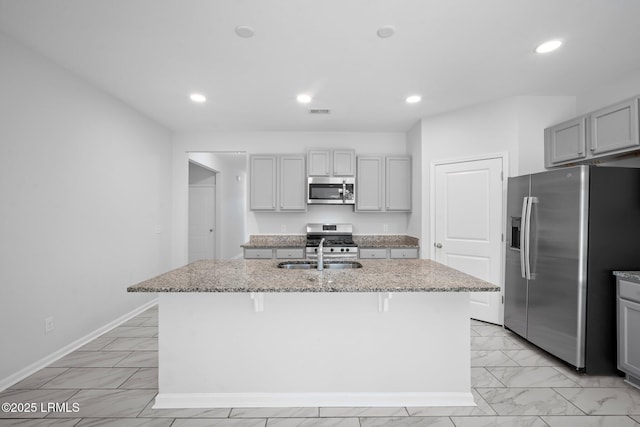 kitchen featuring sink, gray cabinets, a center island with sink, stainless steel appliances, and a kitchen bar