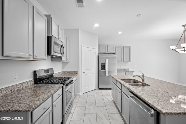 kitchen featuring sink, gray cabinetry, hanging light fixtures, appliances with stainless steel finishes, and dark stone counters