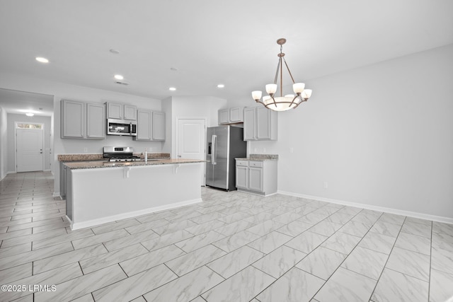 kitchen with gray cabinetry, decorative light fixtures, a notable chandelier, stainless steel appliances, and a kitchen island with sink