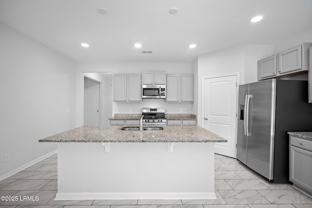 kitchen featuring appliances with stainless steel finishes, gray cabinetry, a center island with sink, and sink