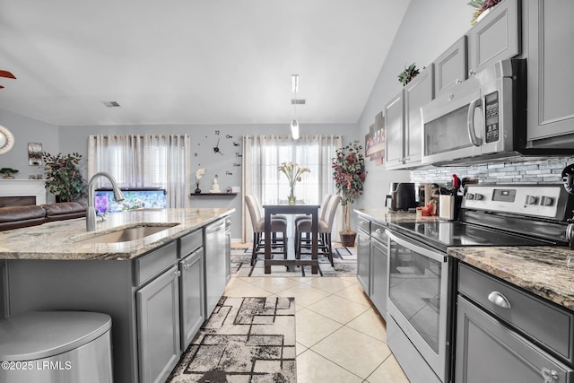 kitchen with light tile patterned flooring, gray cabinetry, stainless steel appliances, a sink, and an island with sink