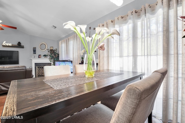 dining space featuring a fireplace, visible vents, and vaulted ceiling